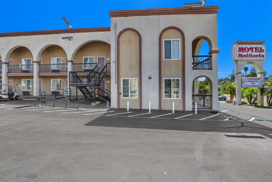 Two-story exterior corridor and stairwell with motel sign and parking area
